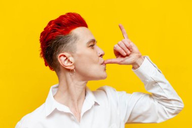 Genç, kısa saçlı, gülümseyen ve sarı yalıtılmış arka planda jumbo jestler yapan bir kız. Piercing takan ve Shaka hareketi yapan bir hipster kadın.