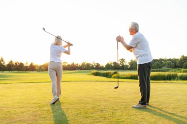 Yaşlı çift golf sahasında golf oynuyor ve gün batımında sohbet ediyor. Yaşlı erkek ve kadın dışarıda dinleniyor ve gülüyor. Emekliler tatilde.