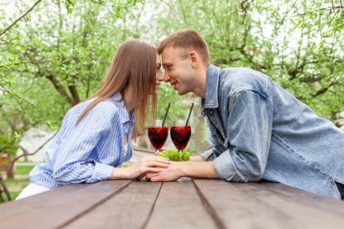 Kot elbiseli genç bir çift, tahta bir masada oturmuş, yazın bir randevuda üzümlü kırmızı şarap içiyorlar, erkek ve kız alkollü kokteyller deniyor ve flört ediyorlar.