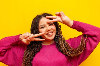 Sarıya boyanmış arka planda barış jesti gösteren, rastalı gülüşlü, tombul Afrikalı Amerikalı kadın artı iki parmaklı, uzun saçlı, uzun boylu bir kız.