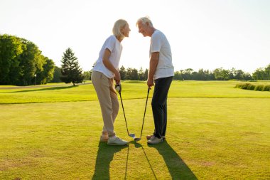 Yaşlı çift golf sahasında golf oynuyor ve gün batımında sohbet ediyor. Yaşlı erkek ve kadın dışarıda dinleniyor ve gülüyor. Emekliler tatilde.