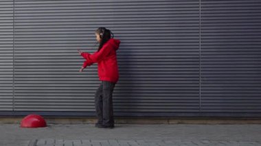 Kırmızı kapüşonlu genç kız kulaklıkla müzik dinliyor ve sokakta ay yürüyüşü yapıyor, enerjik kadın hip hop dansçısı şehrin arka planında duvarın arkasında dans ediyor.