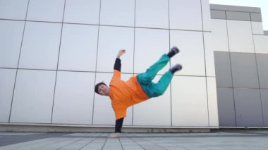 Genç ve enerjik dansçı adam sokakta arka planda dans ediyor erkek akrobat ekstrem numaralar yapıyor ve hip-hop dansı yapıyor.