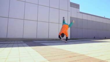 Genç ve enerjik dansçı adam sokakta arka planda dans ediyor erkek akrobat ekstrem numaralar yapıyor ve hip-hop dansı yapıyor.