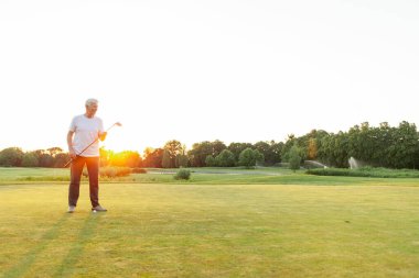 Gri saçlı, golf oynayan ve golf kulübünü elinde tutan yaşlı bir adam. Kıdemli işadamı gün batımında spor yapıyor ve dinleniyor.