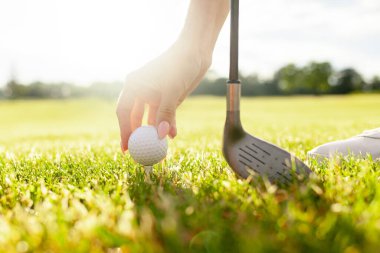 Genç kız golf sahasında golf oynar ve topu atışın altına atar, golfçülerin el ve sopalarını çimlerin ve günbatımının arka planına yakın plan çekerler.