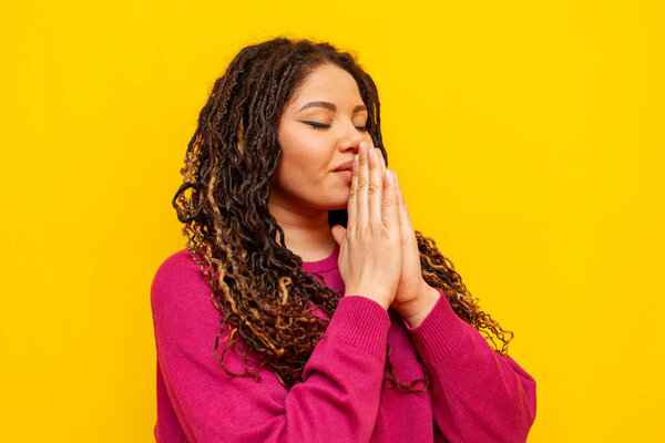 plump african american woman praying and asking god for help on yellow isolated background, big plus size girl with dreadlocks hoping and believing