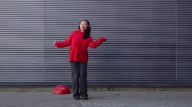 Kırmızı kapüşonlu genç kız kulaklıkla müzik dinliyor ve sokakta dans ediyor, enerjik kadın hip hop dansçısı şehrin arka planında duvarın arkasında dans ediyor.
