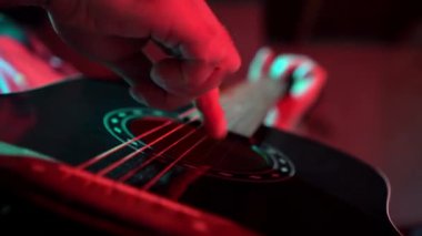 Adam gece akustik gitar çalıyor, müzisyen akorları değiştiriyor ve yakın çekim müzik aletinin tellerinde şarkı çalıyor.