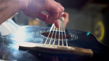 Adam akustik gitar çalıyor ve parmaklarıyla tellere dokunuyor. Müzisyen siyah gitarla müzik çalıyor.