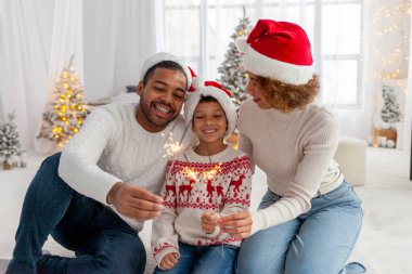 Noel Baba şapkalı Afro-Amerikan ailesi yılbaşını birlikte kutluyor ve Noel ağacının yanında evde maytap tutuyor, anne baba ve küçük oğlu Noel 'de eğleniyor.