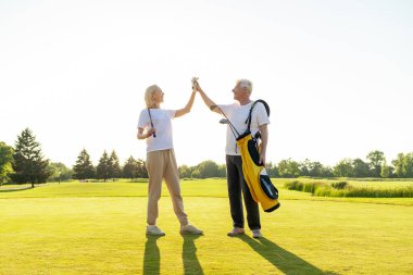 Üniformalı yaşlı çift golf oyununda zaferi ve başarıyı kutluyor ve gün batımında golf oynayan yaşlı adam ve kadına beşlik çakıyor ve açık hava sporları yapıyor.