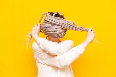 Siyah saçlı, korkmuş genç bir kız sarı arka planda panik içinde bağırıyor ve saçlarını örgü ve saç stilinde benzersiz bir şekilde strese sokuyor.