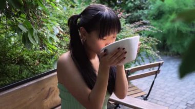 Genç Asyalı kadın açık kafede kaseden ramen içiyor, Koreli kadın kaseden kepçeyle çorba içiyor ve parktaki restoranda höpürdetiyor.