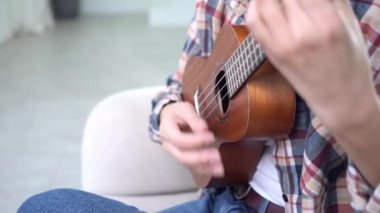 Evde ukulele çalan ve telleri değiştiren genç bir kadın. Yakın plan, akustik gitar çalan bayan müzisyen.