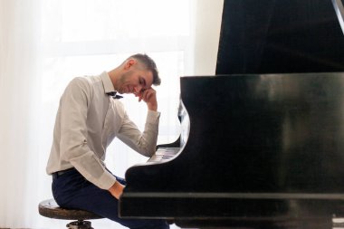 Beyaz gömlekli mutsuz genç adam eski siyah piyanoyu çalıyor ve üzgün, hayal kırıklığına uğramış müzisyen depresyondaki akustik müzik enstrümanında melodi çalıyor.
