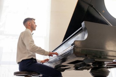 Beyaz gömlekli genç adam eski siyah piyanoyla çalar, müzisyen piyanist akustik müzik enstrümanında melodi çalar.