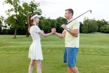 Sahada golf oynayıp el sıkışan genç ve sportif çift, erkek ve kadın, golf yarışmasında tezahürat yapıyor ve yarışıyor ve takım çalışması hareketleri sergiliyor.
