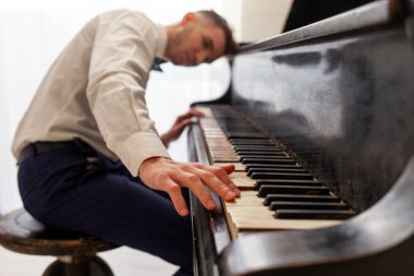 Beyaz gömlekli genç adam eski siyah piyanoyla çalar, müzisyen piyanist akustik müzik enstrümanında melodi çalar.