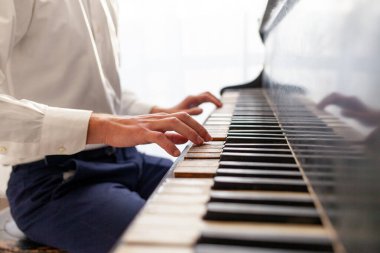 Beyaz gömlekli genç adam eski siyah piyanoyu çalıyor, müzisyen akustik müzik enstrümanında melodi çalıyor, yakın plan.