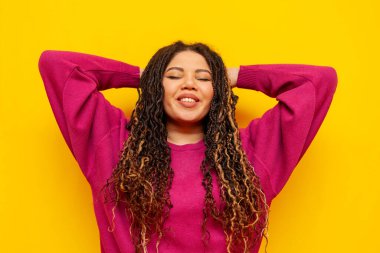 Saçları örgülü, sarı izole edilmiş arka planda dinlenen neşeli, tombul Afro-Amerikan kadını. Rasta saçlı iri yarı, elleri başının arkasında uzanmış bir kız.