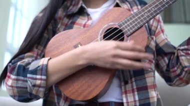 Evde ukulele çalan ve telleri değiştiren genç bir kadın. Yakın plan, akustik gitar çalan bayan müzisyen.