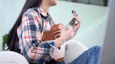 Evde ukulele çalan ve telleri değiştiren genç bir kadın. Yakın plan, akustik gitar çalan bayan müzisyen.