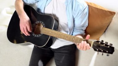 Gömlekli sakallı adam evde siyah akustik gitar çalıyor, müzisyen içeride müzik aleti kullanıyor ve şarkı söylüyor, yakın plan.