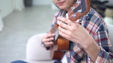 Evde ukulele çalan ve telleri değiştiren genç bir kadın. Yakın plan, akustik gitar çalan bayan müzisyen.