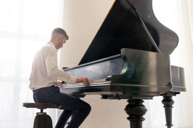 Beyaz gömlekli genç adam eski siyah piyanoyla çalar, müzisyen piyanist akustik müzik enstrümanında melodi çalar.