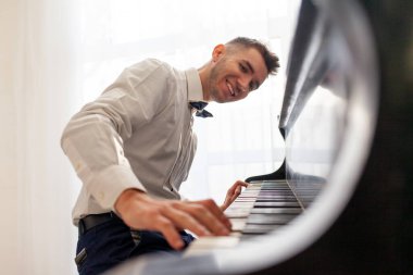 Beyaz gömlekli genç adam eski siyah piyanoyla çalar, müzisyen piyanist akustik müzik enstrümanında melodi çalar.