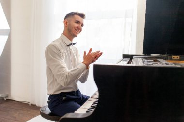Beyaz gömlekli genç adam eski siyah piyano ve alkış çalıyor, müzisyen akustik müzik enstrümanında melodi çalıyor.