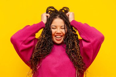 Saçları örgülü neşeli, tombul Afro-Amerikan kadın saçlarını tutuyor ve sarı yalıtılmış arka planda gülümsüyor. Rasta saçlı, iri yarı, iri yarı bir kız.