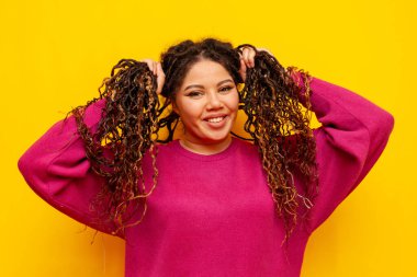 Saçları örgülü neşeli, tombul Afro-Amerikan kadın saçlarını tutuyor ve sarı yalıtılmış arka planda gülümsüyor. Rasta saçlı, iri yarı, iri yarı bir kız.