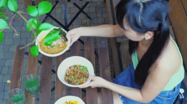 Genç, neşeli Asyalı kadın ramen ve pilav karıştırıyor açık kafede yemek çubuklarıyla, kadın parktaki restoranda erişte yiyor, yakın plan.