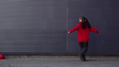 Kırmızı kapüşonlu neşeli genç Asyalı kız şehrin arka planında yürüyor ve seviniyor. Koreli kadın dışarıda yürüyor ve dönüyor.