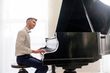 Beyaz gömlekli genç adam eski siyah piyanoyla çalar, müzisyen piyanist akustik müzik enstrümanında melodi çalar.