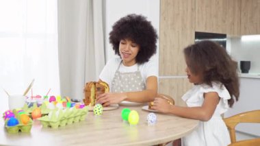 Afro-Amerikan anne ve kızı Paskalya 'yı kutluyor ve evde paskalya pastası yiyor, çocuklu kadın pasta yiyor ve masada yumurta boyuyor.