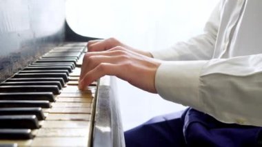 Beyaz gömlekli genç adam piyanoda klasik müzik çalıyor, müzisyen müzik aletinde melodi çalıyor, yakın plan.
