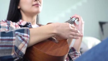 Evde ukulele çalan ve telleri değiştiren genç bir kadın. Yakın plan, akustik gitar çalan bayan müzisyen.