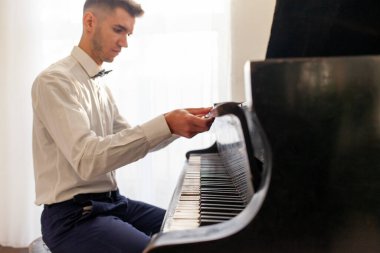 Beyaz gömlekli genç adam eski siyah piyanoyla çalar, müzisyen piyanist akustik müzik enstrümanında melodi çalar.