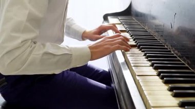 Beyaz gömlekli genç adam piyanoda klasik müzik çalıyor, müzisyen müzik aletinde melodi çalıyor, yakın plan.