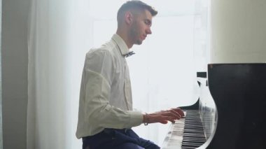 Beyaz gömlekli genç adam piyanoda klasik müzik çalar, müzisyen müzik aletinde melodi çalar.