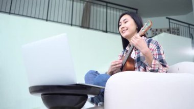 Genç Asyalı bir kadın bilgisayarda ukulele çalmayı öğreniyor Koreli bir kız video dersinden müzik aleti çalmayı öğreniyor.