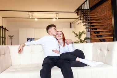 Genç çift kanepede oturup öpüşüyor, kadın ve erkek evdeki rahat ve yumuşak bir kanepede sarılıp dinleniyorlar.