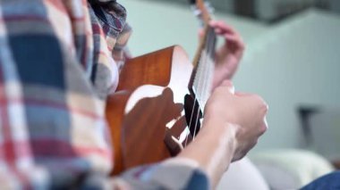 Evde ukulele çalan ve telleri değiştiren genç bir kadın. Yakın plan, akustik gitar çalan bayan müzisyen.