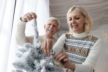 Bir çift yaşlı süveter içinde yeni yılı evde kutluyor ve ağacı süslüyorlar. Gri saçlı yaşlı büyükbaba ve karısı Noel için evi hazırlıyorlar.