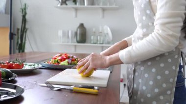 Önlüklü genç Asyalı kadın evdeki mutfakta hazırladığı salataya limon suyu döküyor Koreli kız evde sağlıklı yemekler pişiriyor ve doğranmış sebzelere limon ekliyor.