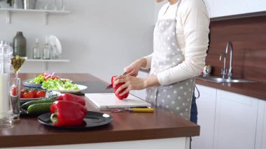 Önlüklü genç Asyalı kadın evde salata için biber kesiyor, Koreli kız evde sağlıklı yemekler pişiriyor ve sebze kesiyor.
