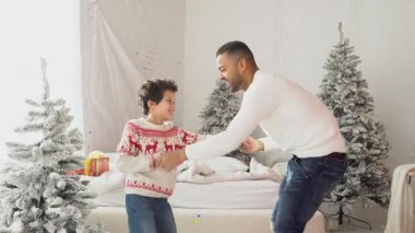 Afro-Amerikan erkek ve oğlu yeni yılı evde kutluyor ve süslerle dans ediyor, çocuk ve baba eğleniyor ve Noel 'de oynuyorlar.